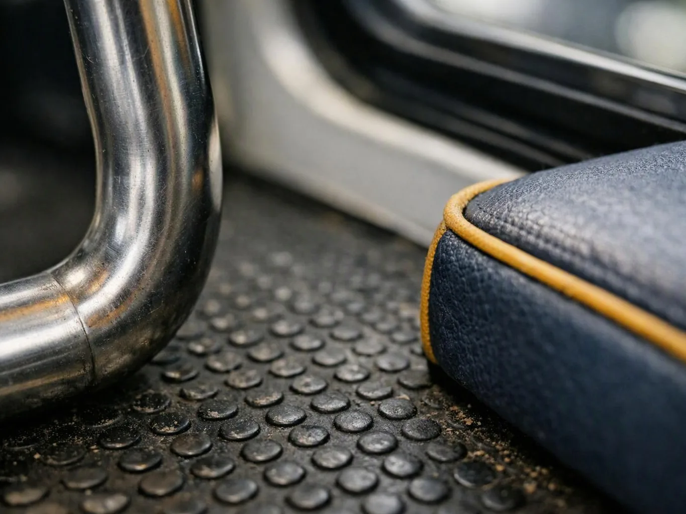 Close-up of a bus or train floor, showing a metal pole and a blue seat edge with yellow piping