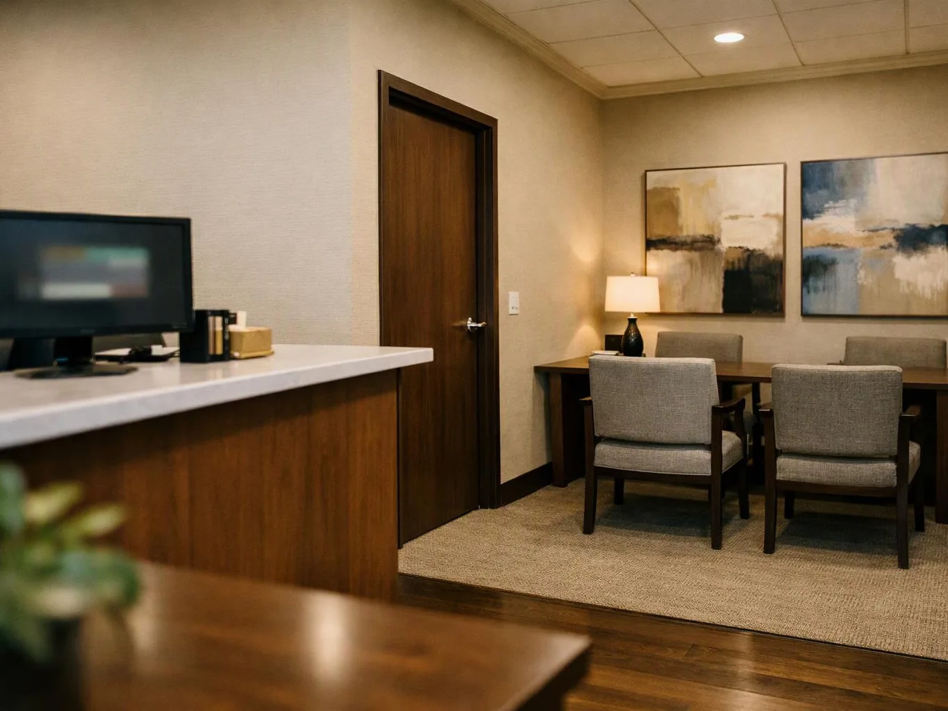 A quiet office lounge shows a desk, wooden door, small lamp, and chairs around a table